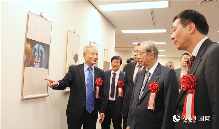 “湖州印象”攝影展主創(chuàng)、世界華人攝影協(xié)會副會長馮學(xué)敏向吳江浩大使、福田康夫前首相等嘉賓介紹展出作品。（人民網(wǎng) 許可攝）