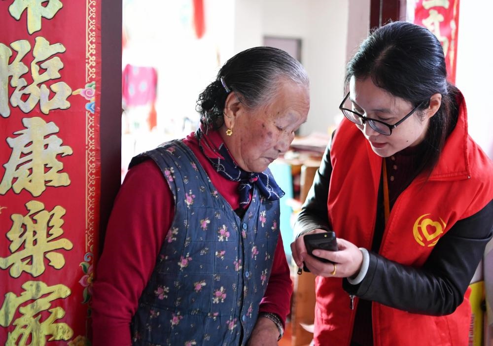 在福州市長樂區(qū)航城街道籌岐村，智慧養(yǎng)老平臺派駐社區(qū)的助老員（右）在為老人陳鳳英（左）講解養(yǎng)老定制手機(jī)的用法（2021年11月26日攝）。新華社記者 魏培全 攝