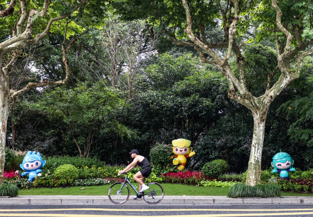 市民在杭州市南山路上一處亞運會主題吉祥物雕塑前騎自行車。