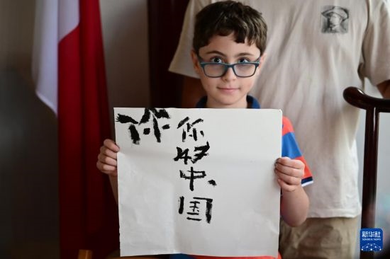 7月4日，在馬耳他桑塔露琪亞市的中國(guó)古典園林“靜園”，一名男孩展示他的書(shū)法作品。新華社發(fā)（喬納森·博格 攝）