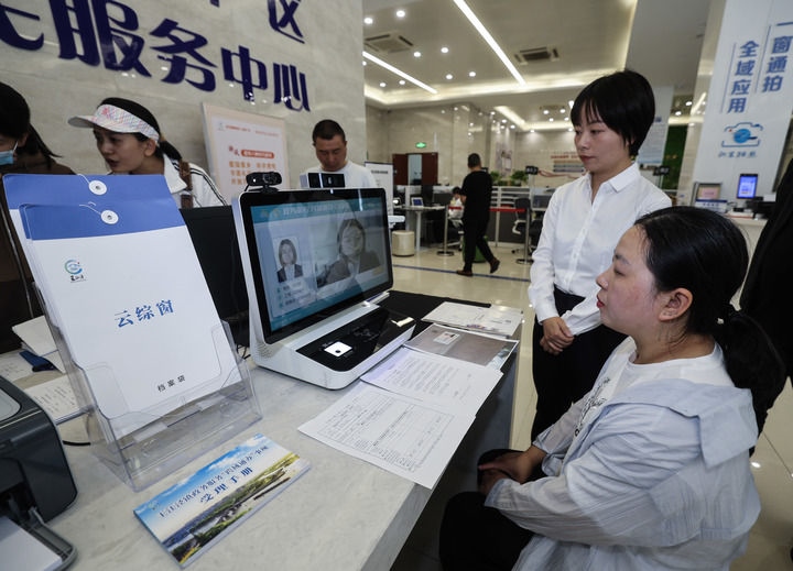 在浙江省嘉興市秀洲區(qū)王江涇鎮(zhèn)便民服務(wù)中心的“跨域通辦·云綜窗”窗口，辦理開(kāi)業(yè)登記的個(gè)體工商戶（右一）通過(guò)該系統(tǒng)與江蘇省蘇州市吳江區(qū)盛澤鎮(zhèn)行政審批局工作人員視頻連線，進(jìn)行身份讀取及材料線上審核（2024年5月9日攝）。新華社記者 徐昱 攝