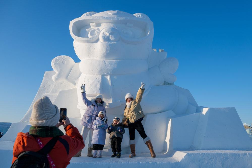 2025年1月3日，在黑龍江哈爾濱冰雪大世界園區(qū)，游客與亞冬會吉祥物雪雕“濱濱”合影
